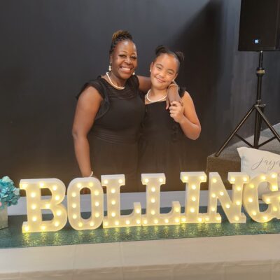 mother and daughter stand behind a celebratory sign saying Bolling, their last name