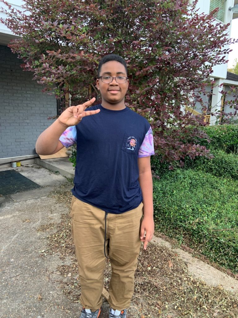 K'Vonnta stands in his front yard and makes a peace sign with his hand.