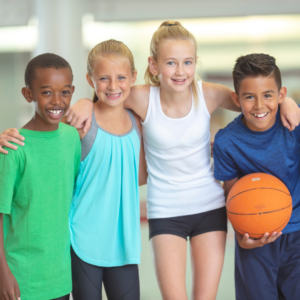 Two girls and 2 boys posing with arms over each others shoulders. One boy is holding a basketball.